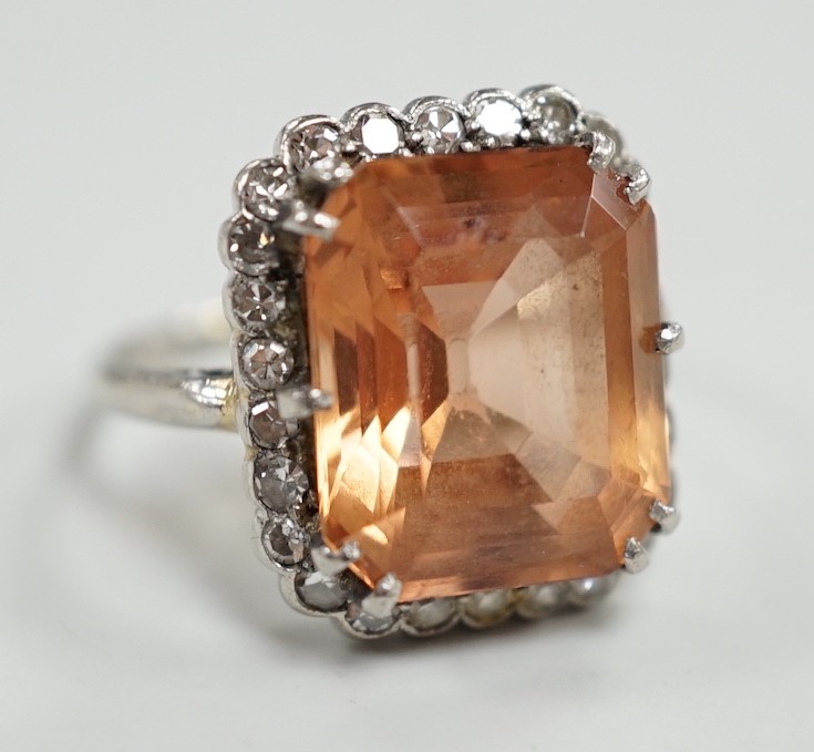 A white metal and emerald cut orange/peach topaz set dress ring, with diamond set border, size I/J, gross weight 6.1 grams.